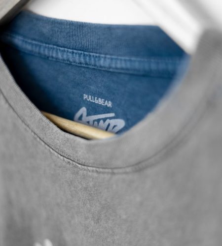 Detailed view of a gray t-shirt with branding, hanging on a wooden hanger.