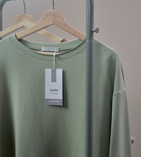 Close-up of a green shirt on a hanger with label tag on a minimalist clothing rack.